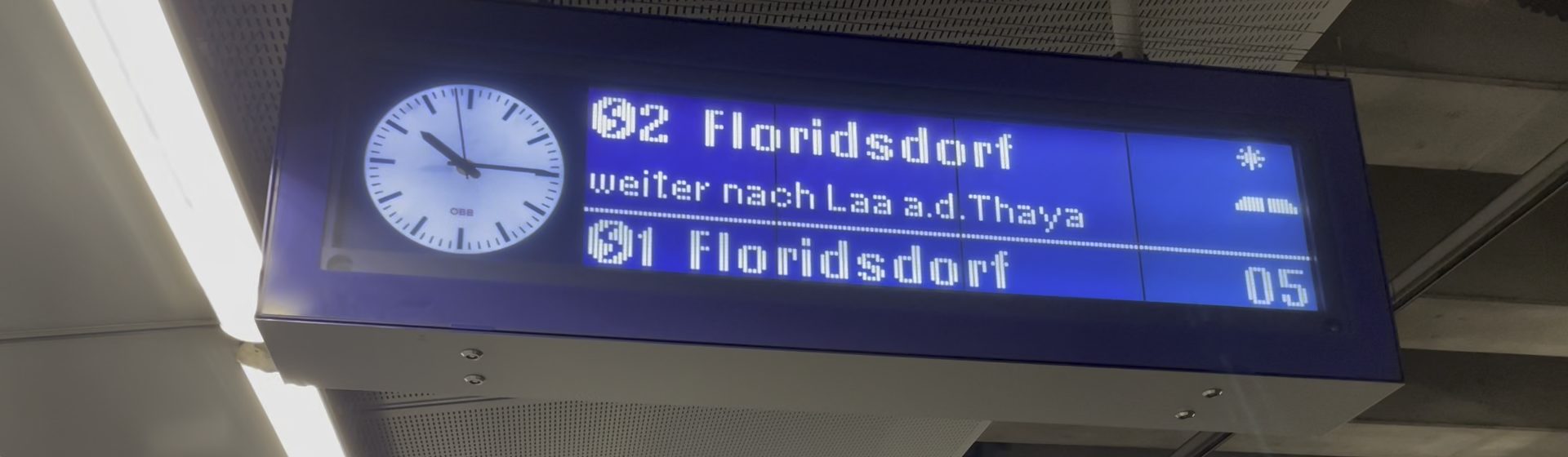 Zuganzeige in einer Wiener S-Bahn-Station mit Uhr und der Aufschrift „02 Floridsdorf, weiter nach Laa a.d. Thaya“ in Punktmatrix-Schrift; rechts oben blinkt ein Sternchen.