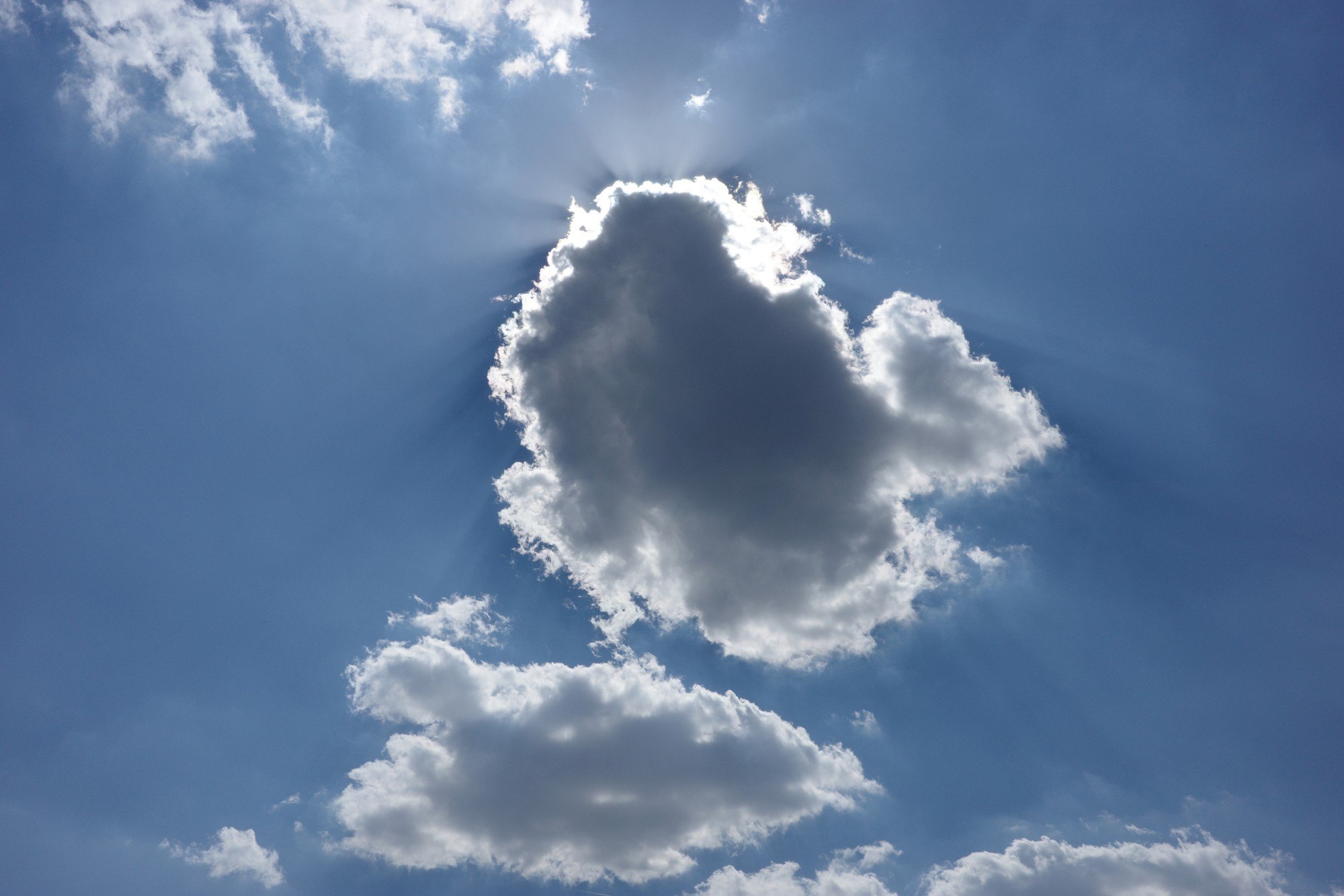 Eine Wolke verdeckt die Sonne, Lichtstrahlen fächern sich hinter ihr in den blauen Himmel.